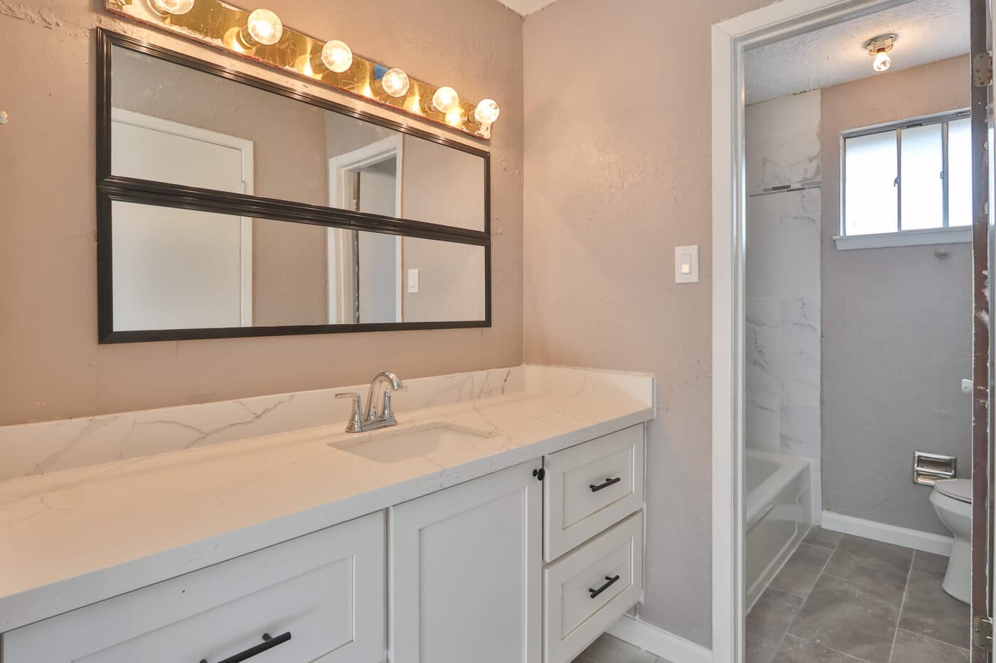 Updated bathroom vanity with white cabinetry and broad mirror